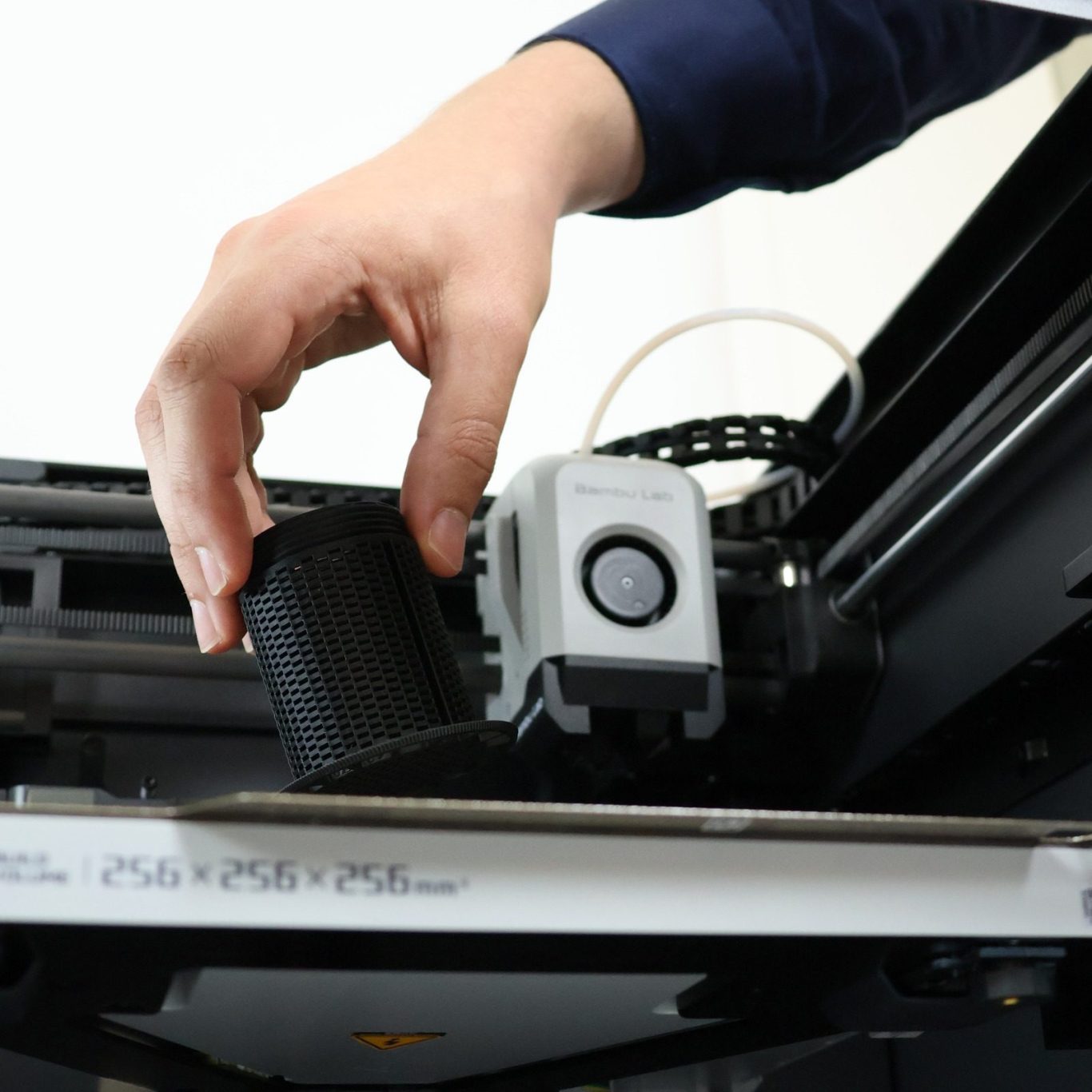 Fertiges Teil wird aus drucker genommen Eine Hand hält ein graues Bauteil an einem Drucker.