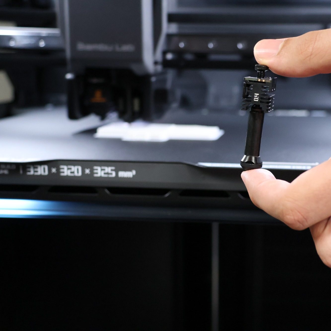 Fast swap Induktions Hotend Hand hält eine kleines Hotend neben einem 3D-Drucker.
